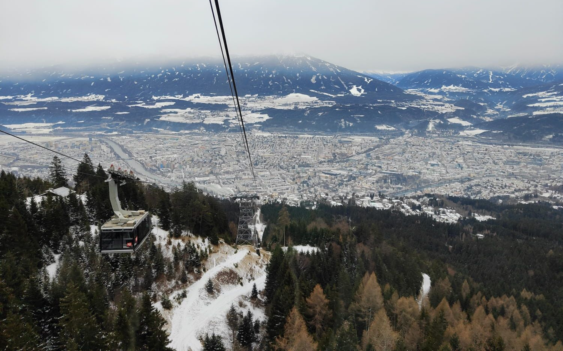Cable car over snowy town and forest, cloudy sky.