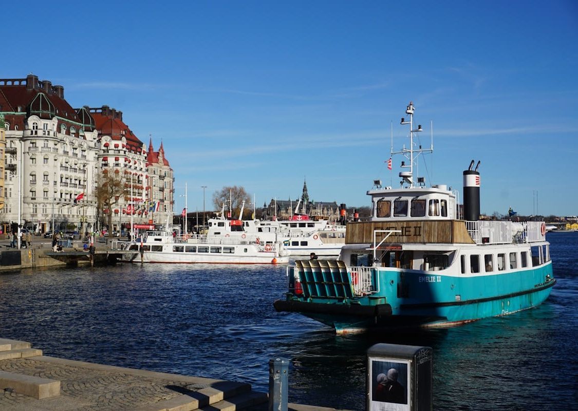 Turquoise ferry on a harbor with waterfront buildings and clear blue sky