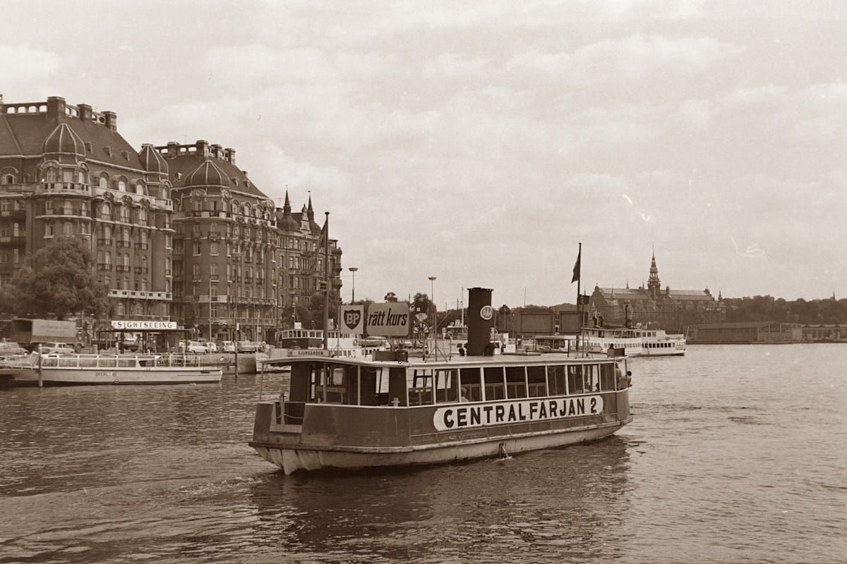 Vintage ferryboat on a river, with historic buildings along the waterfront in the background
