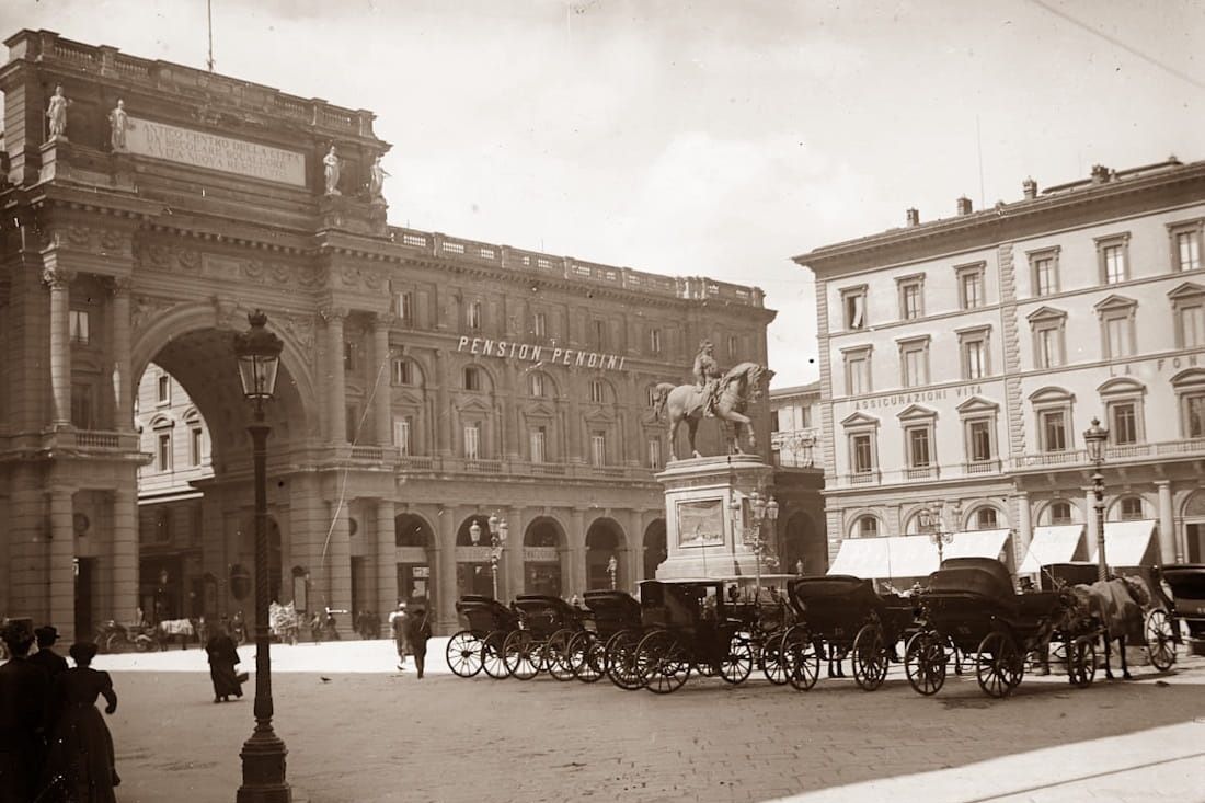 Historic sepia photograph of Piazza della Repubblica in Florence with a central equestrian statue and horse-drawn carriages.