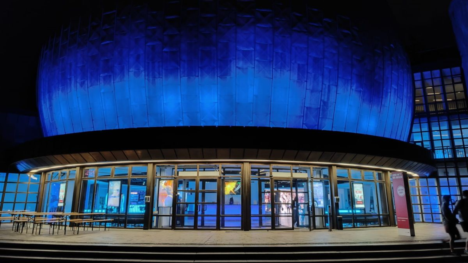 Planetarium Berlin Blue-lit, dome-shaped building entrance at night. Circular overhang above glass doors.