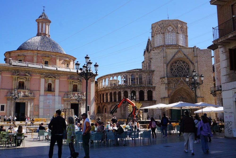 View of Valencia Cathedral and plaza with people, cafes, and construction equipment on a sunny day.