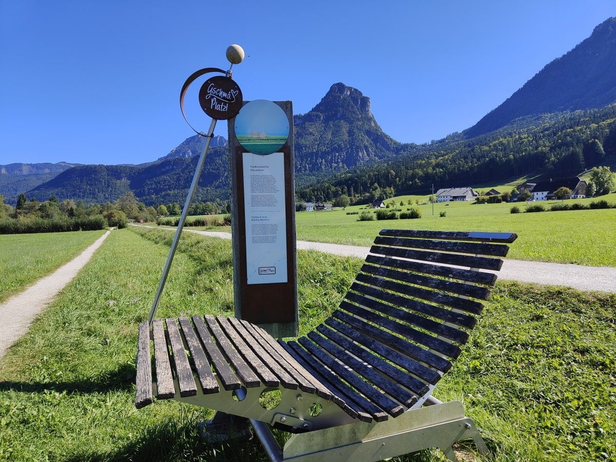 Wooden lounge chair by a sign with a mountain backdrop on a sunny day.