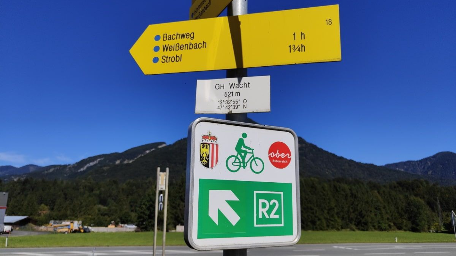 Yellow directional sign and bike route marker, with mountain backdrop under blue sky.