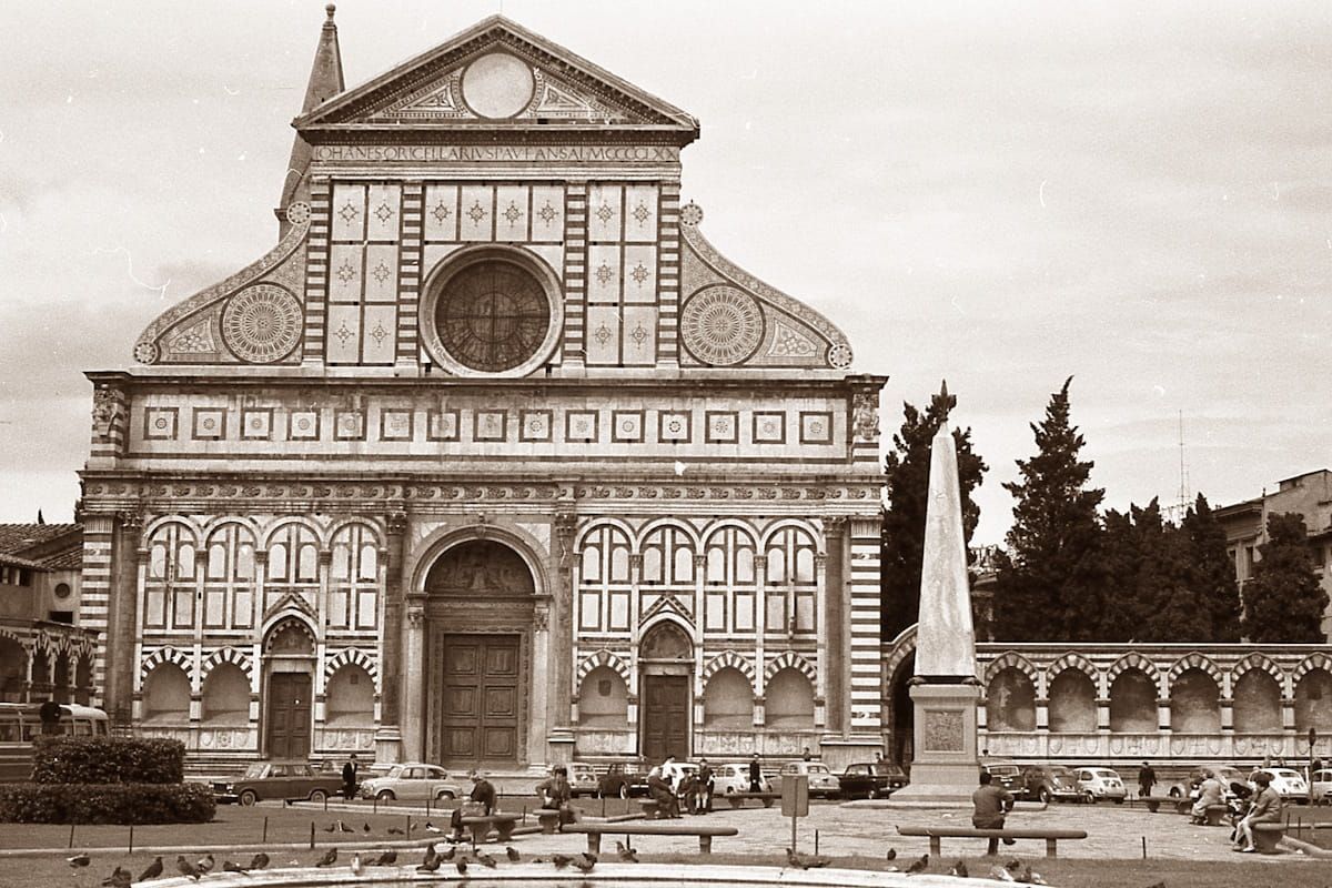 The facade of Santa Maria Novella in Florence, Italy, featuring ornate geometric marble patterns, an obelisk, and trees.