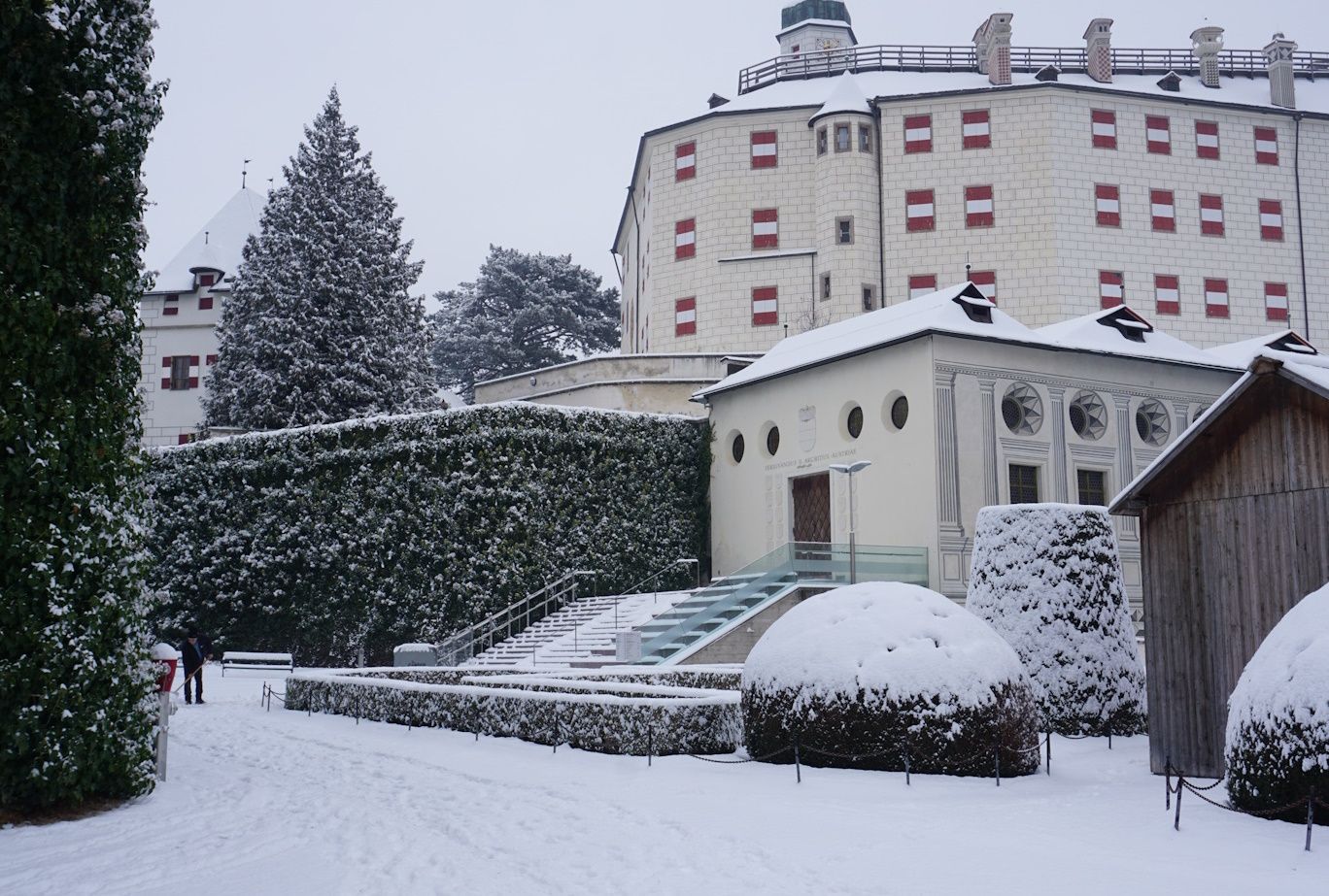 Snowy scene with a castle in the background, a small building and pruned bushes in the foreground.