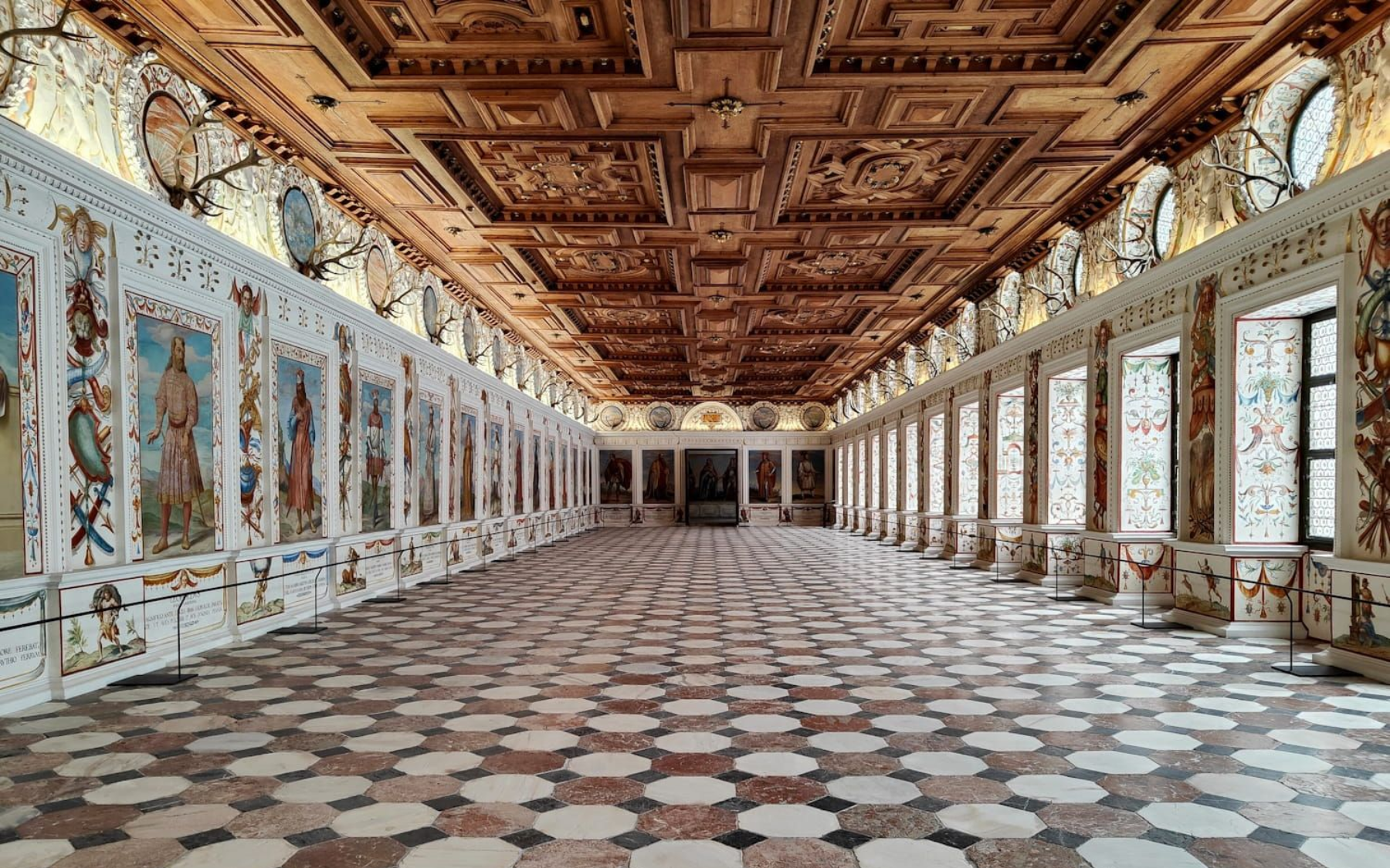 Long, ornate hall with patterned floor, decorated walls, and carved wooden ceiling.