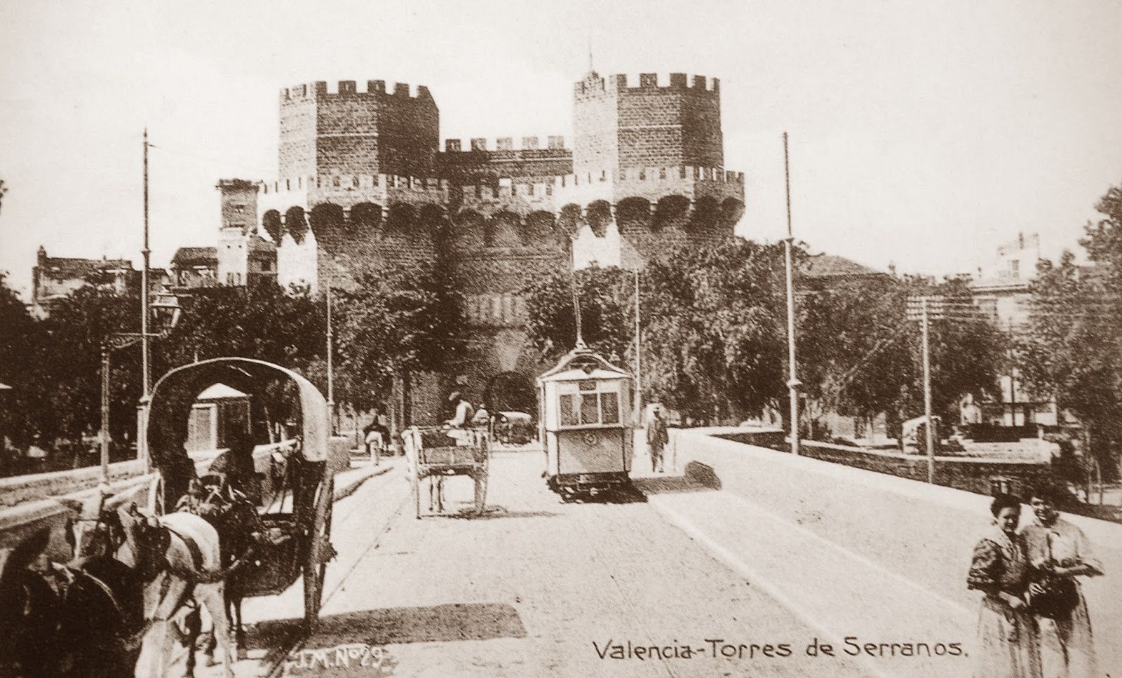 Historical view of Serrano Towers in Valencia, Spain; horse-drawn carriage and tram on street.