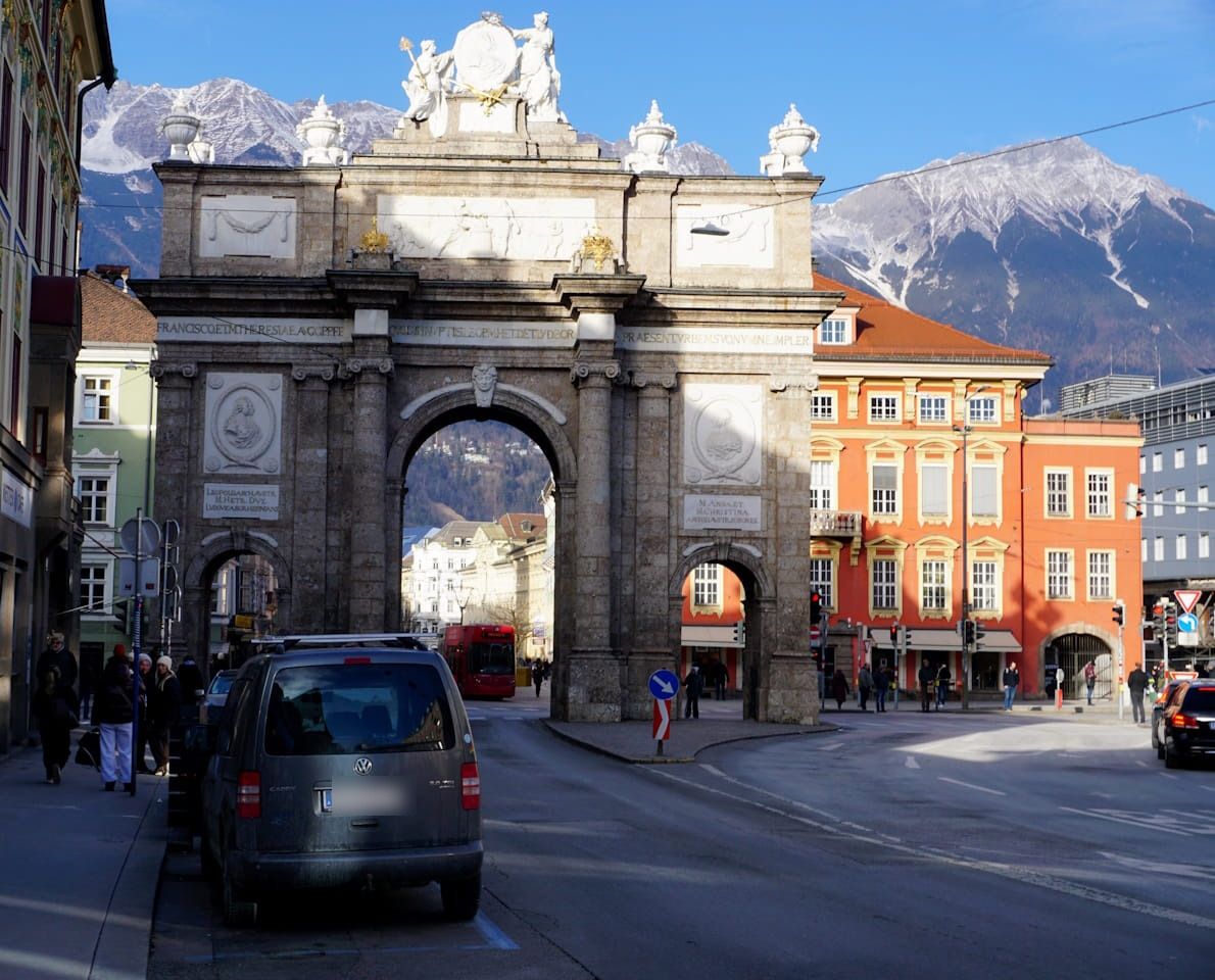 Triumphal arch in Innsbruck, Austria, with mountains in the background. Buildings and cars line the streets.