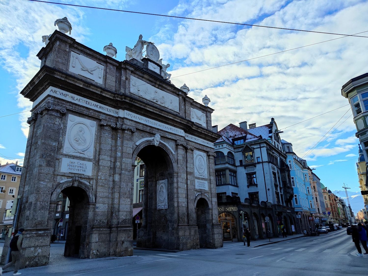 Triumphal arch of Innsbruck, Austria, with city street and cloudy sky background.