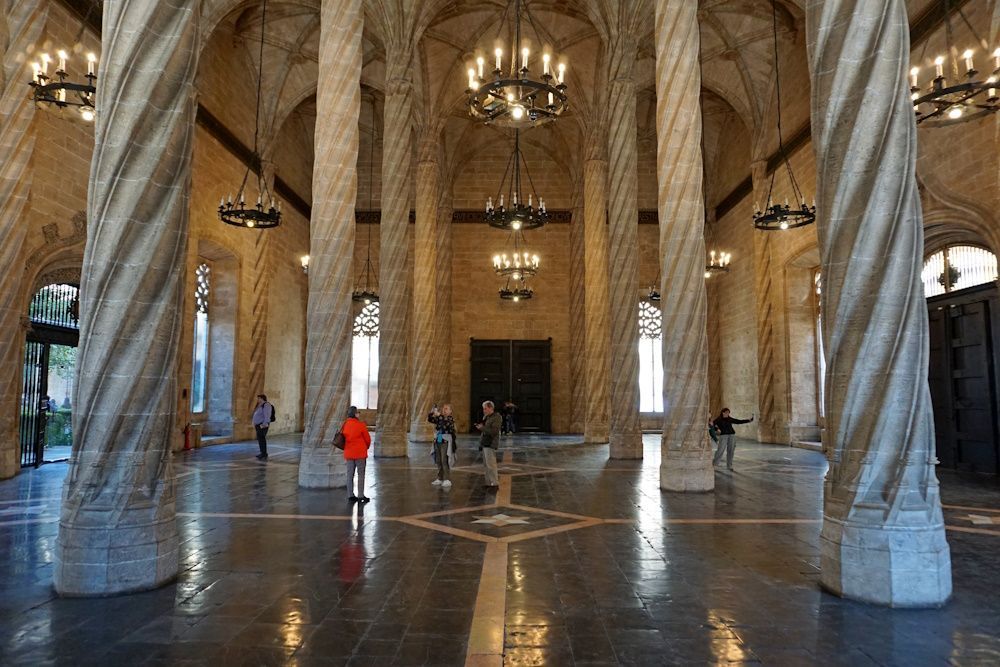 Grand hall with large, spiral columns and arched ceiling. Several people stand on the stone floor.