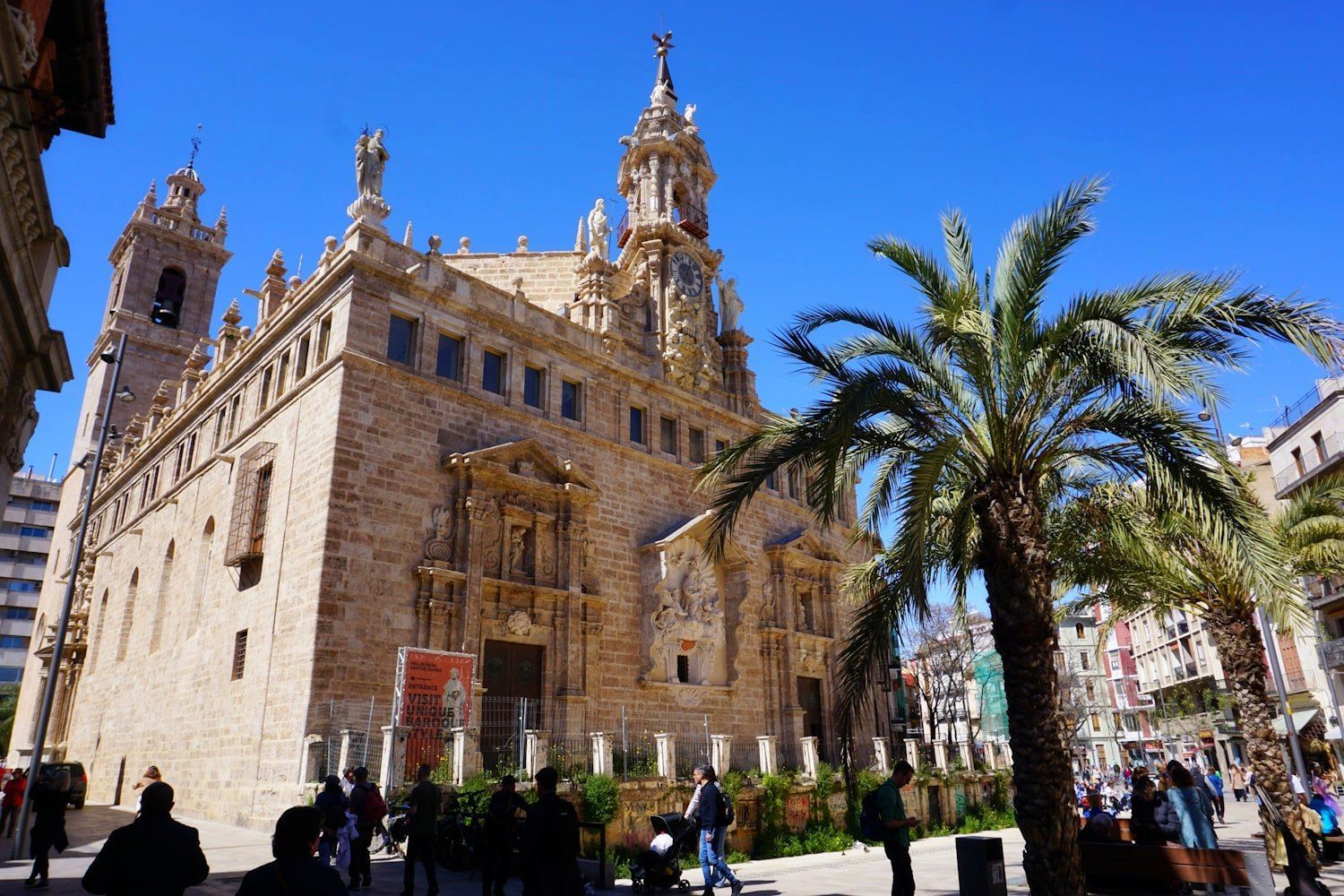 A large ornate building with detailed stonework and a palm tree under a blue sky, Valencia.