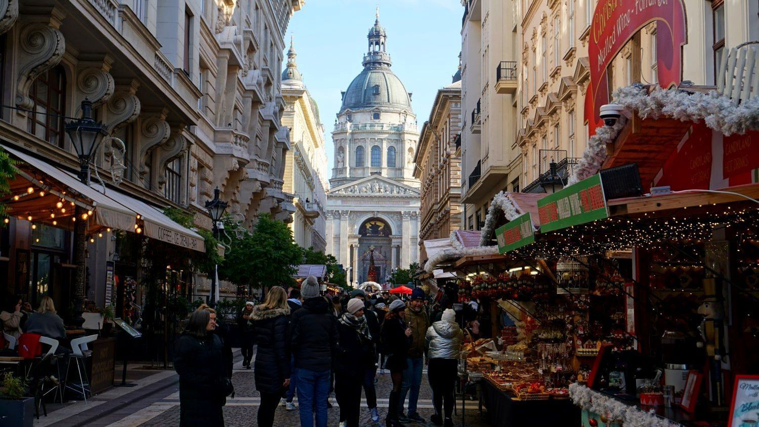 A group of people are walking down a street with a large dome in the background