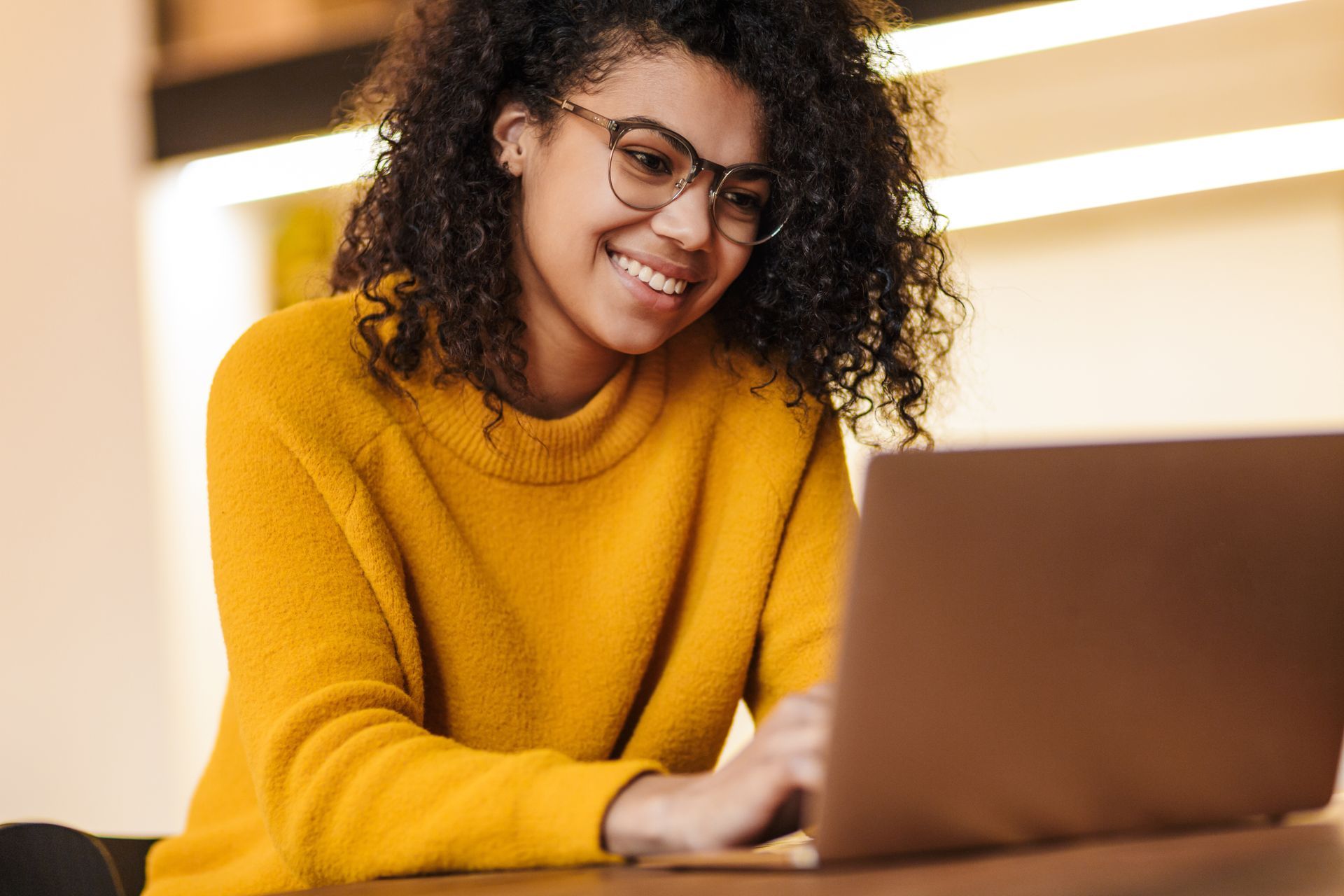 A woman in a yellow sweater is sitting at a table using a laptop computer.