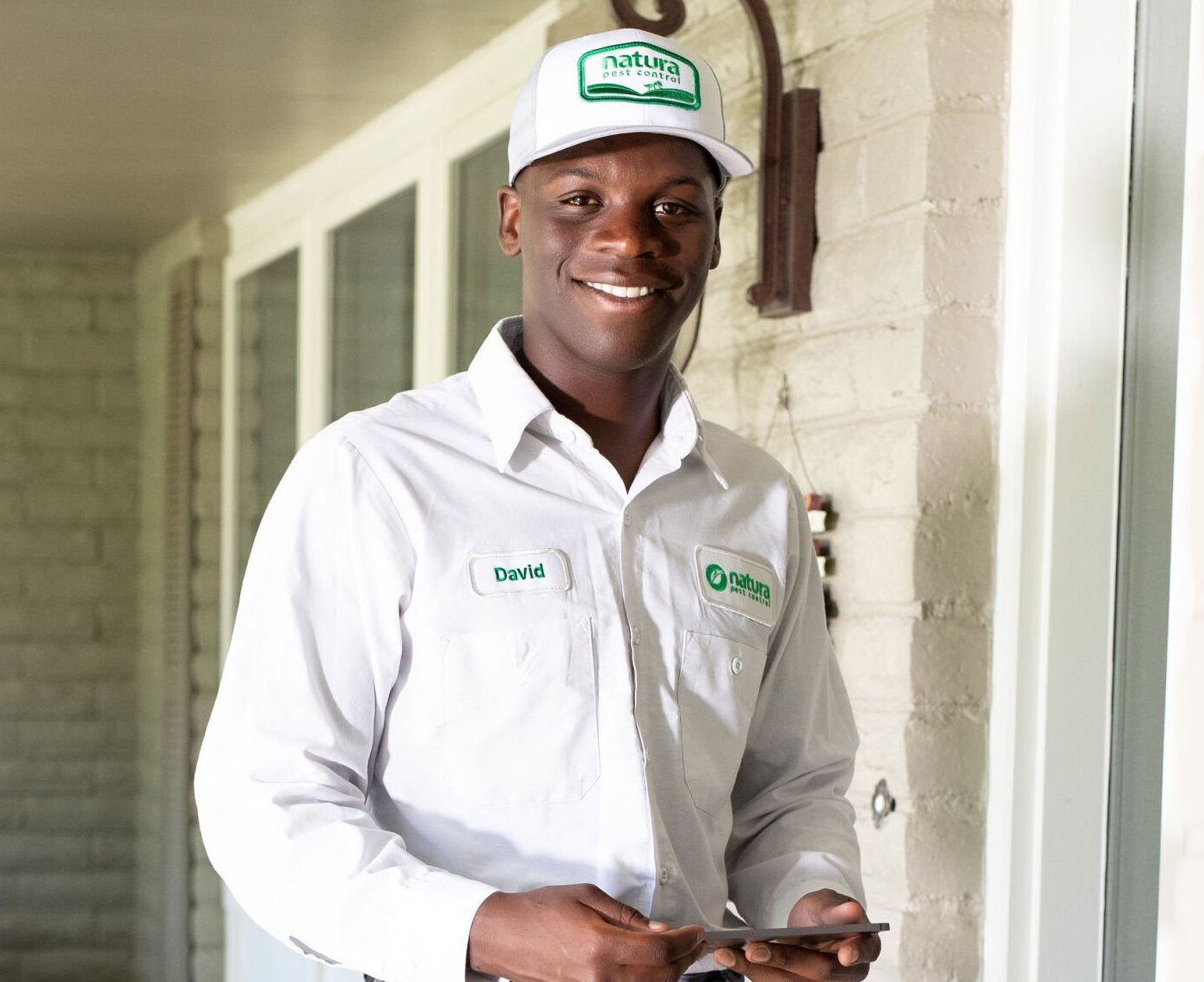 A man wearing a white shirt and a green hat is standing in front of a door holding a cell phone.