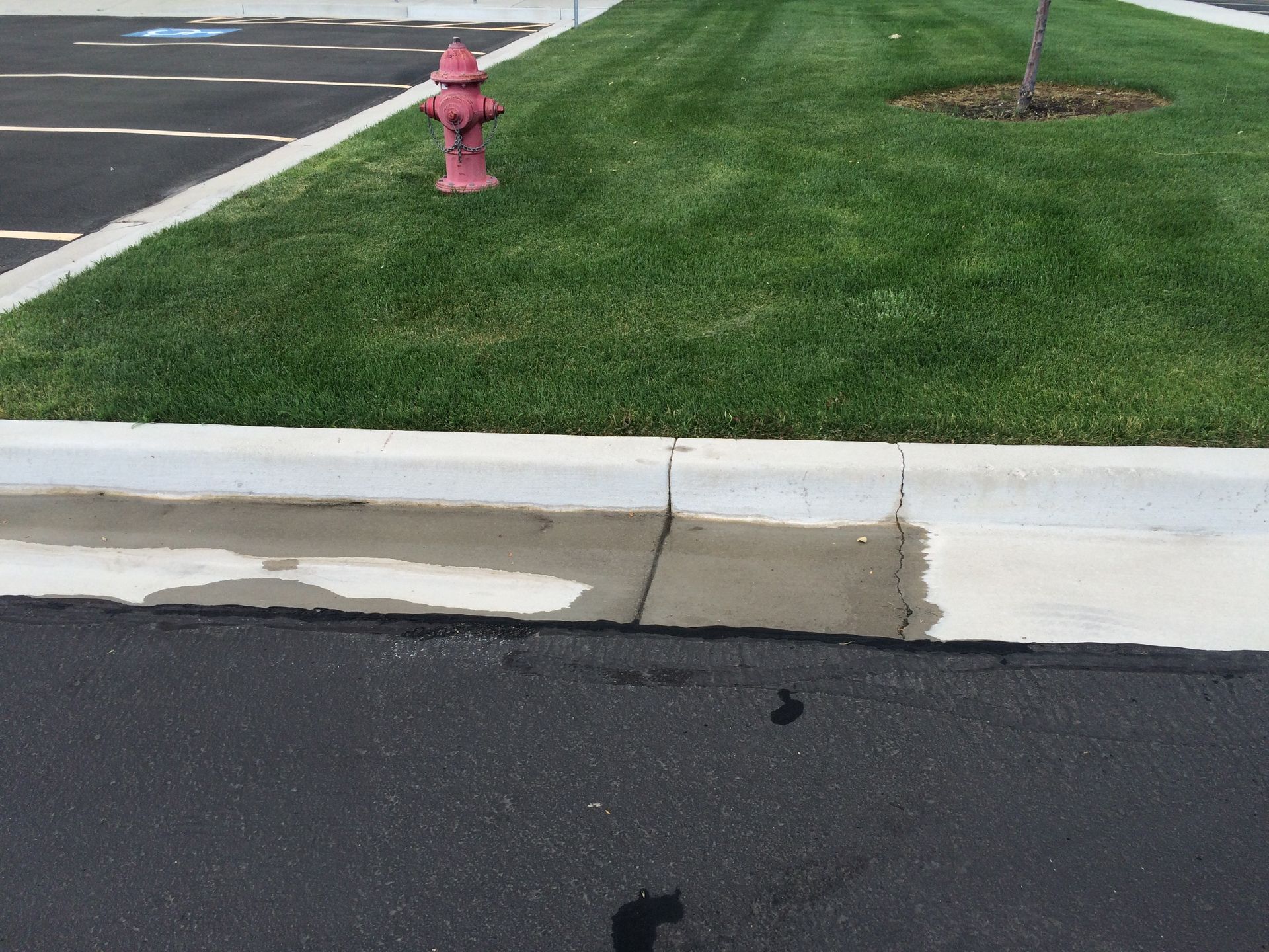 Red fire hydrant near green grass and a concrete curb, next to a black asphalt parking lot.