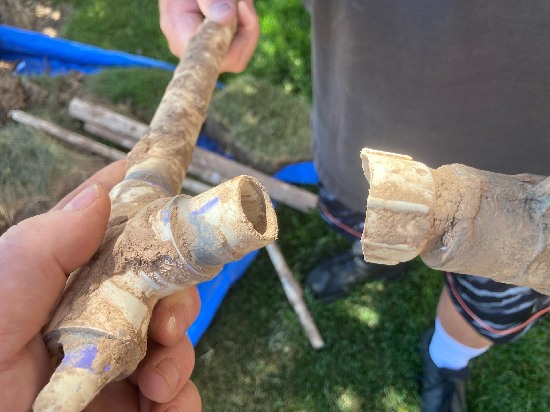 Broken PVC pipe held by a person's hands, outdoors.