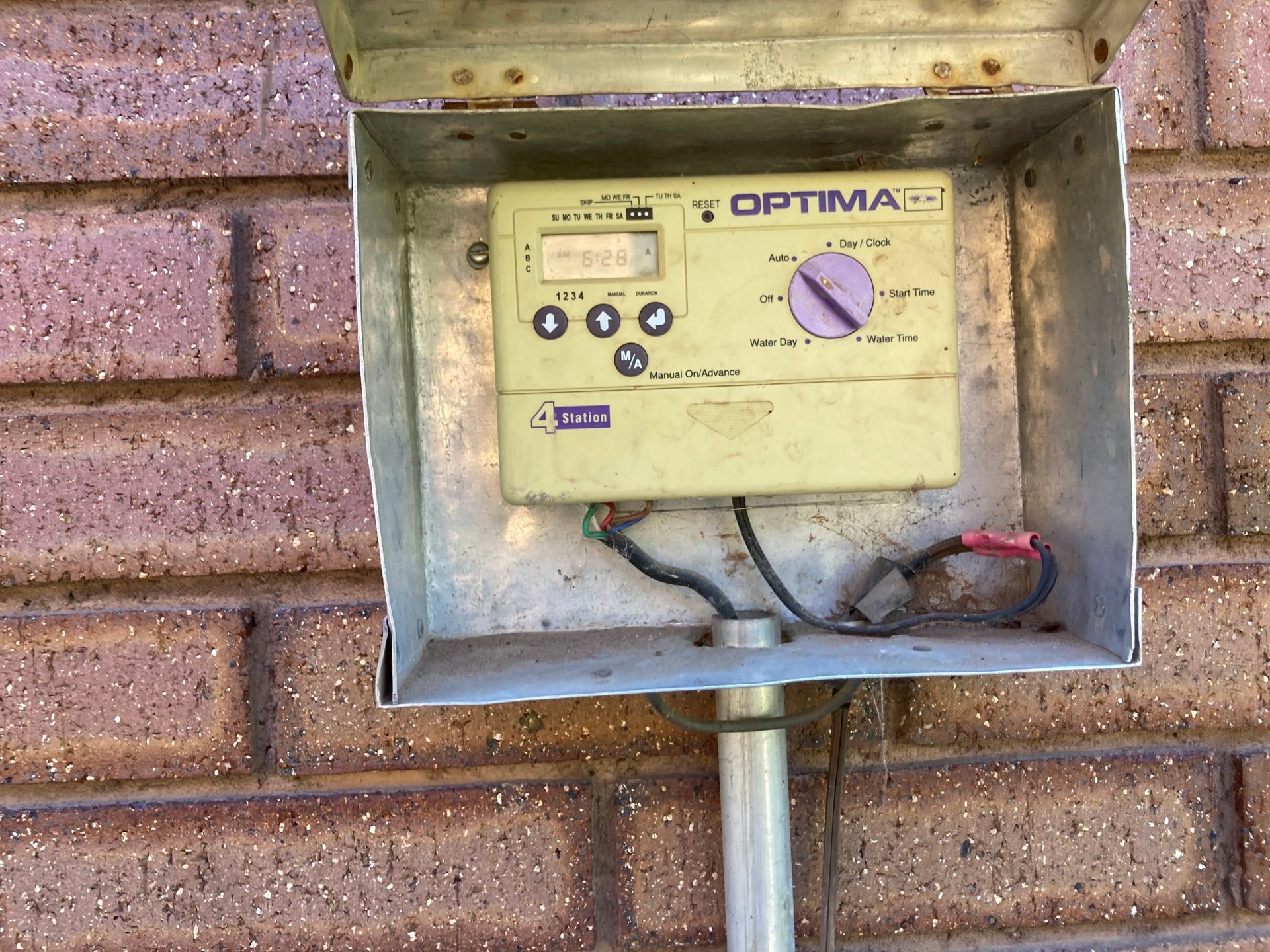 Outdoor Optima sprinkler timer mounted on a brick wall in a metal box.