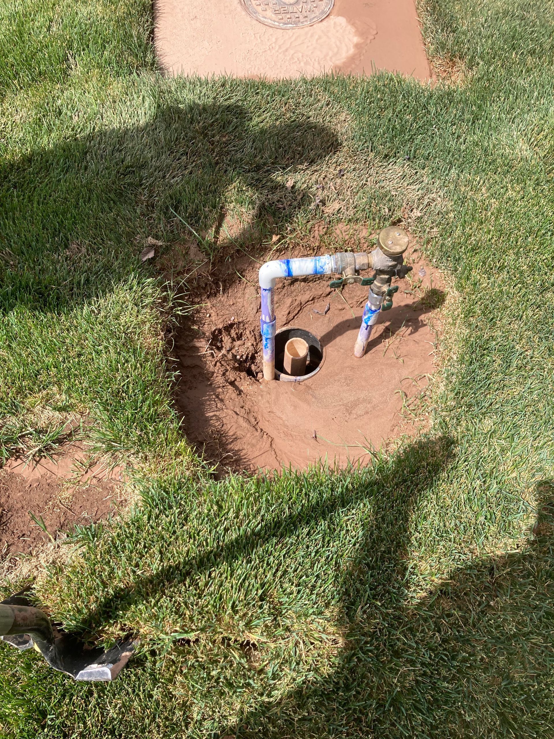 Sprinkler watering green grass in a yard, with trees in the blurry background.