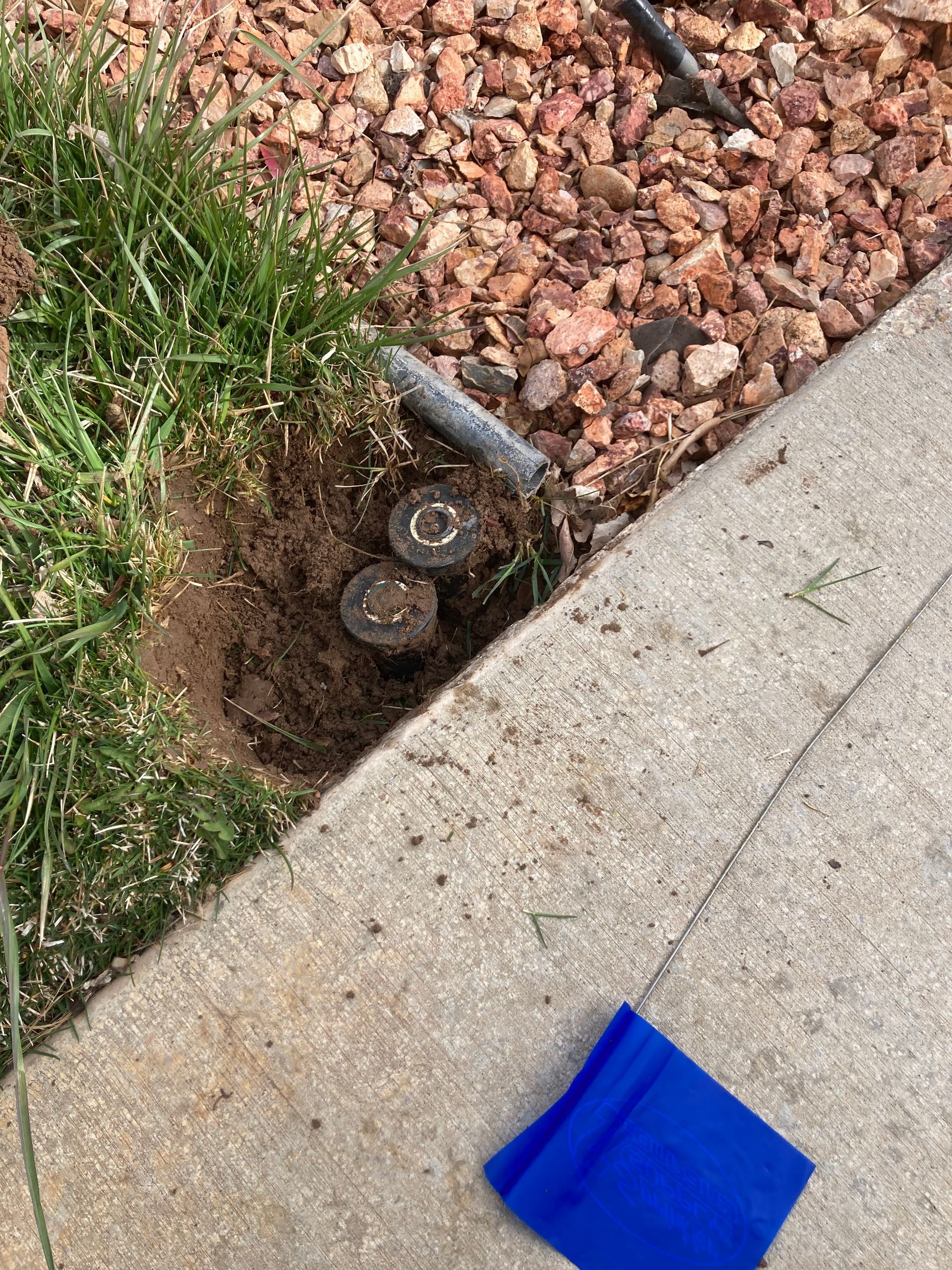 Two sprinkler heads in dirt next to a concrete sidewalk and red gravel.
