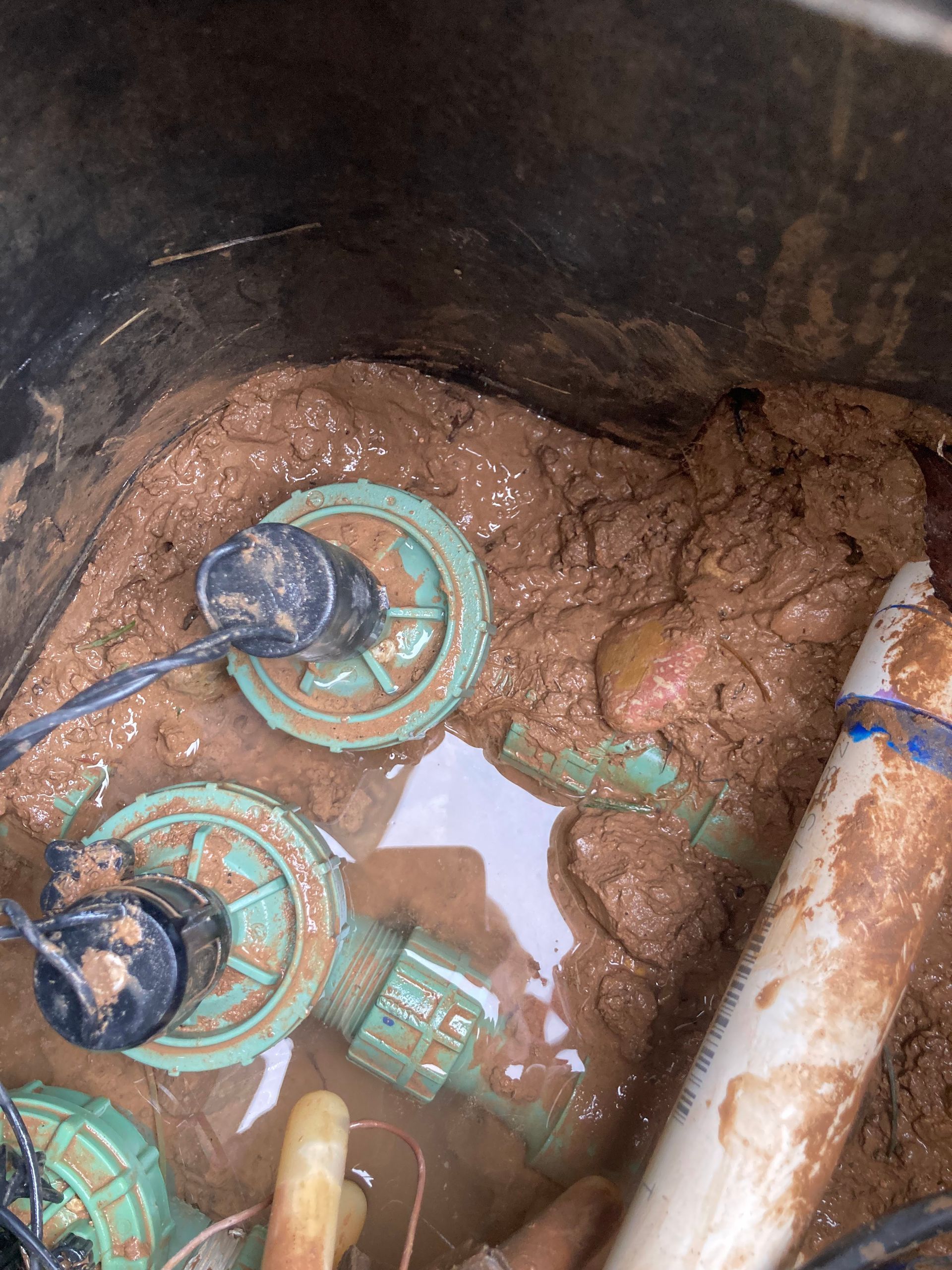 Irrigation valve box filled with mud and water, showing green valves, white pipe.