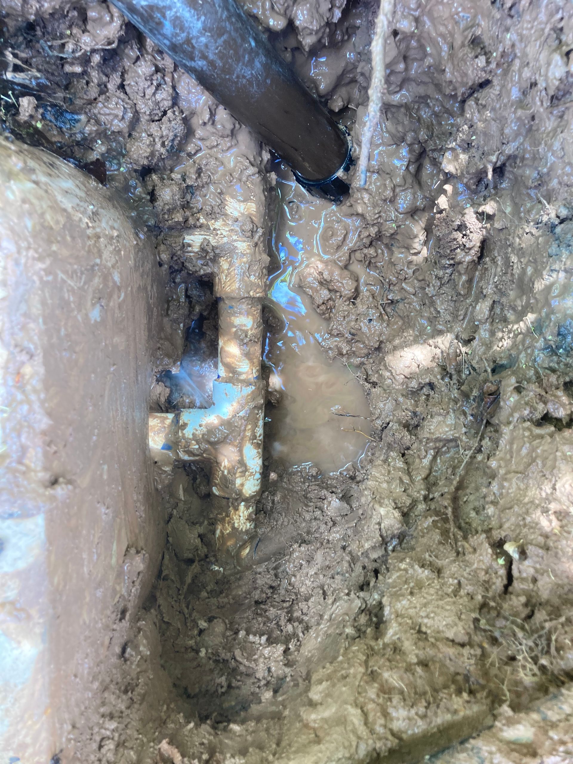 Water leaking from a buried pipe fitting in muddy soil.