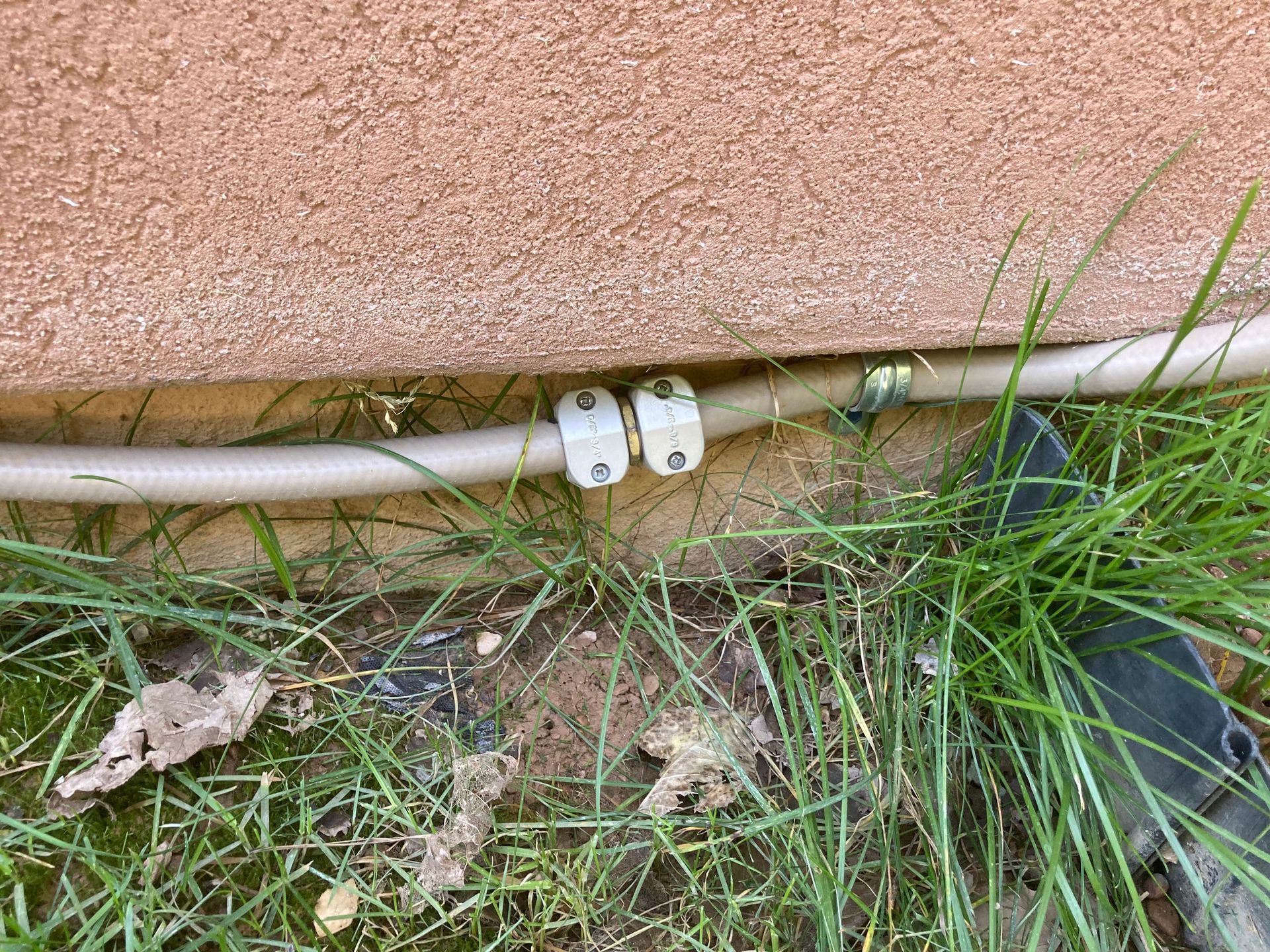 A hose with white clips rests on the ground next to a stucco wall and grass.
