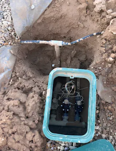 Open irrigation valve box with valves and wires; buried water line with a coupler.