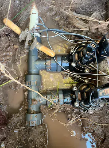 Irrigation system components buried in muddy ground, including valves, pipes, and wiring.
