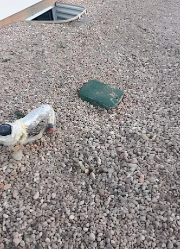 Gravel-covered ground with a green box and a silver pipe, likely part of a building's infrastructure.