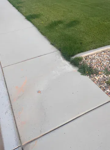 Concrete sidewalk next to grass and gravel. The edge of the sidewalk has some damage and a dirt stain.