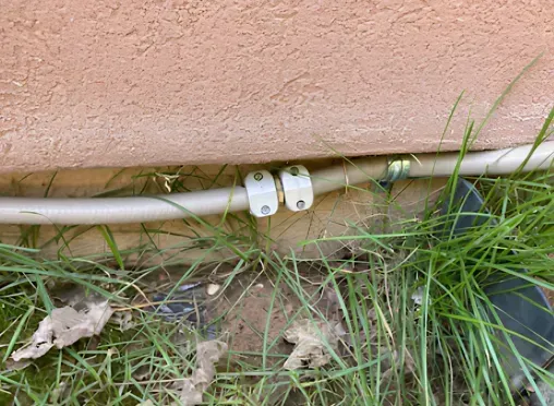 White clamps securing a light-colored hose against a peach-colored wall, surrounded by grass.