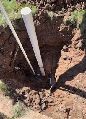 Excavation pit with white PVC pipes, blue connectors, and dirt; outdoors.