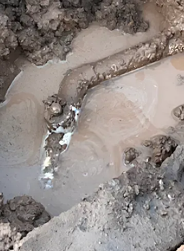 A damaged pipe partially submerged in muddy water, with white residue around the break.
