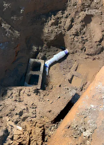 PVC pipe connected to a concrete block in a dirt pit.