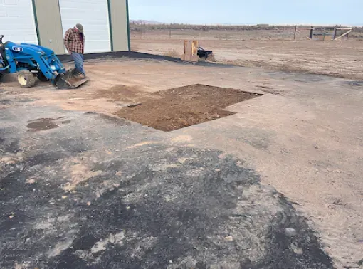 Man and tractor at a building, excavating a section of paved ground.