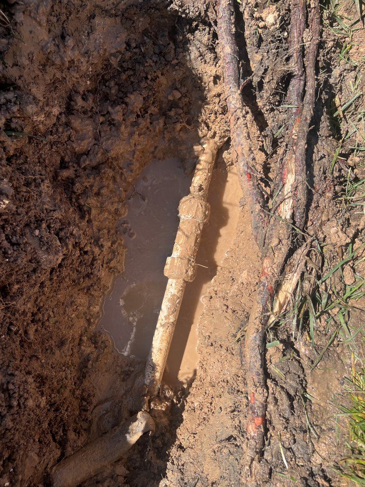 Leaking pipe in a muddy trench, water pooling.