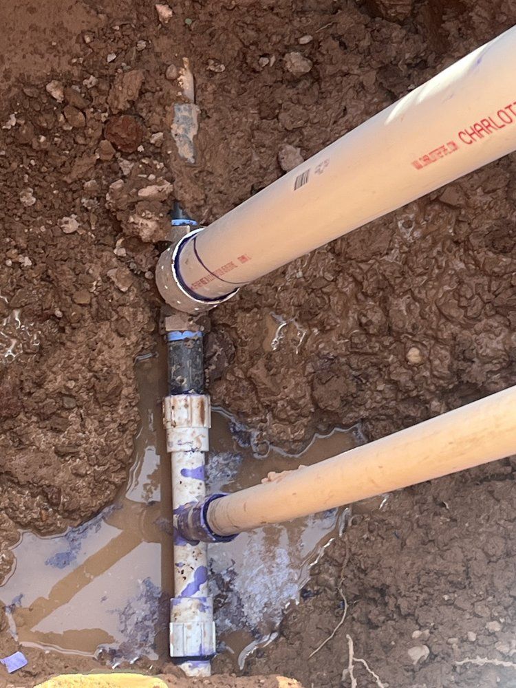 Pipes in a dirt trench, with water present. Two large white pipes connected to a black and white pipe fitting.