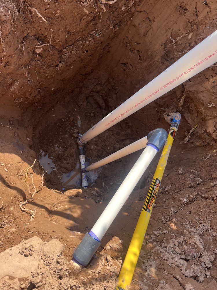 Exposed colored wires and a PVC pipe in dirt, likely part of an underground sprinkler system.