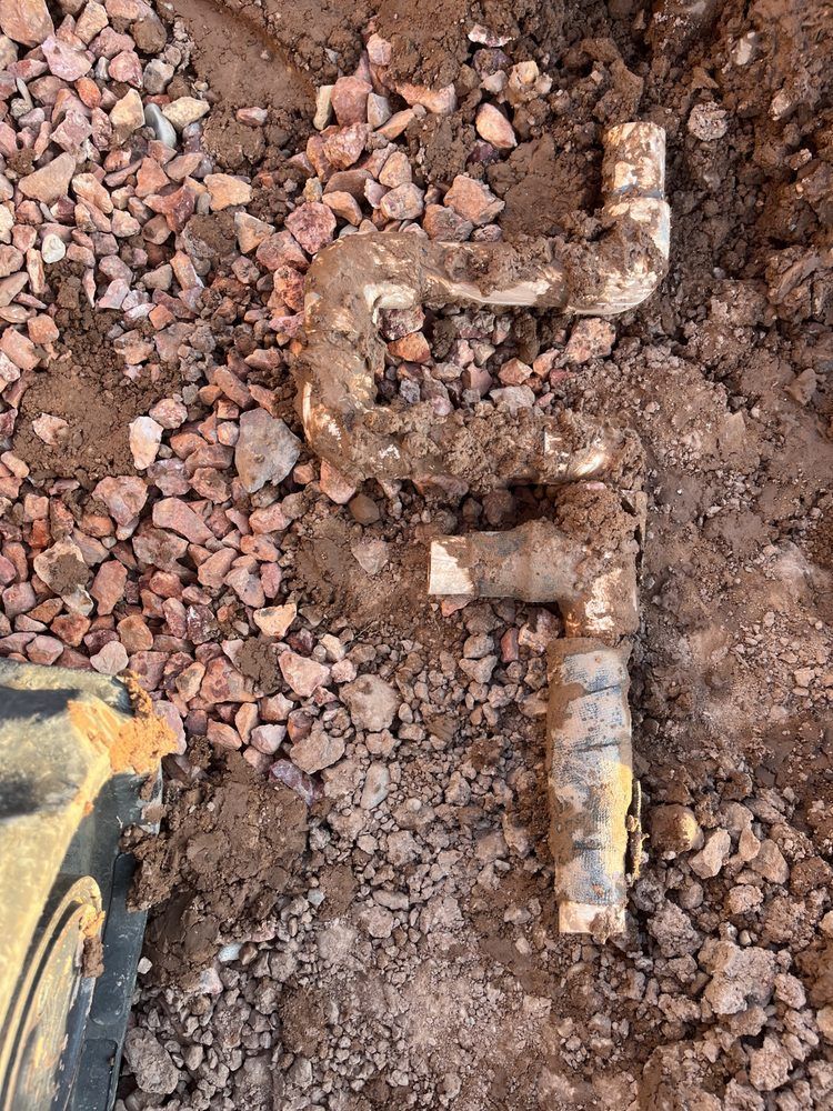 White PVC pipes in a muddy excavation. Brown soil and rocks surround the pipes.