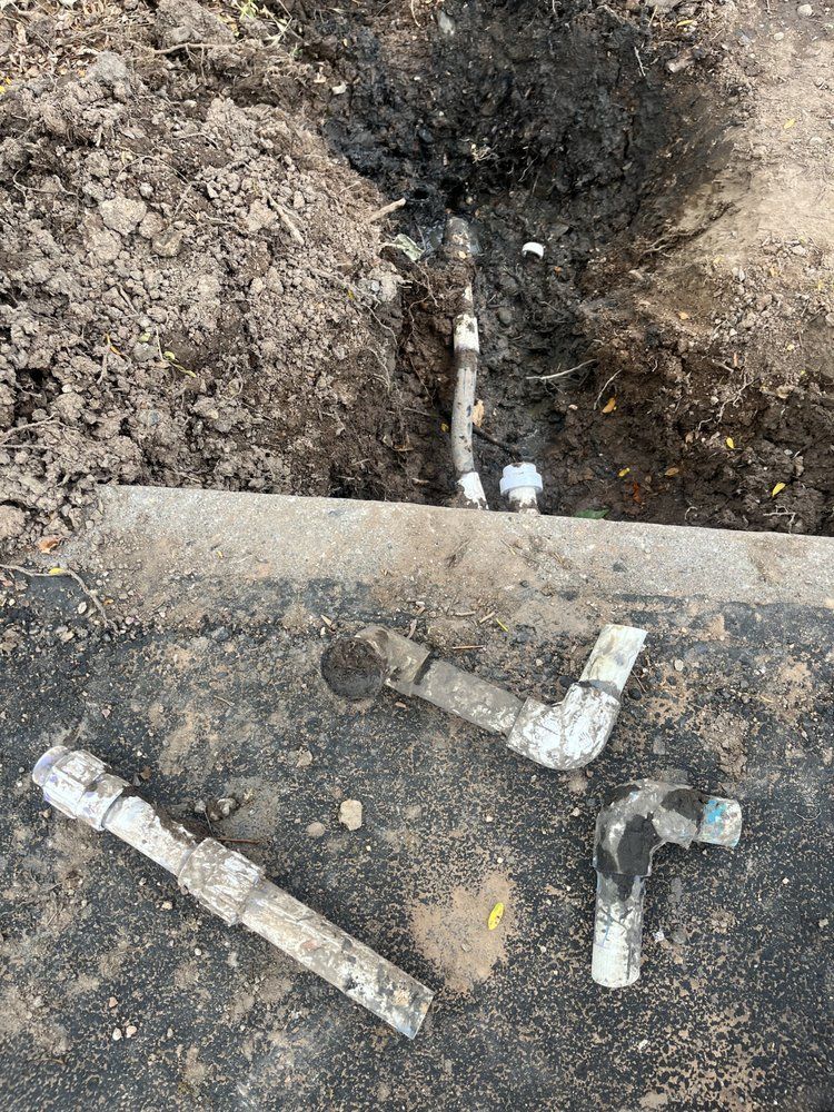 Excavated pipes in dirt. Cut PVC pipes lie nearby on asphalt.