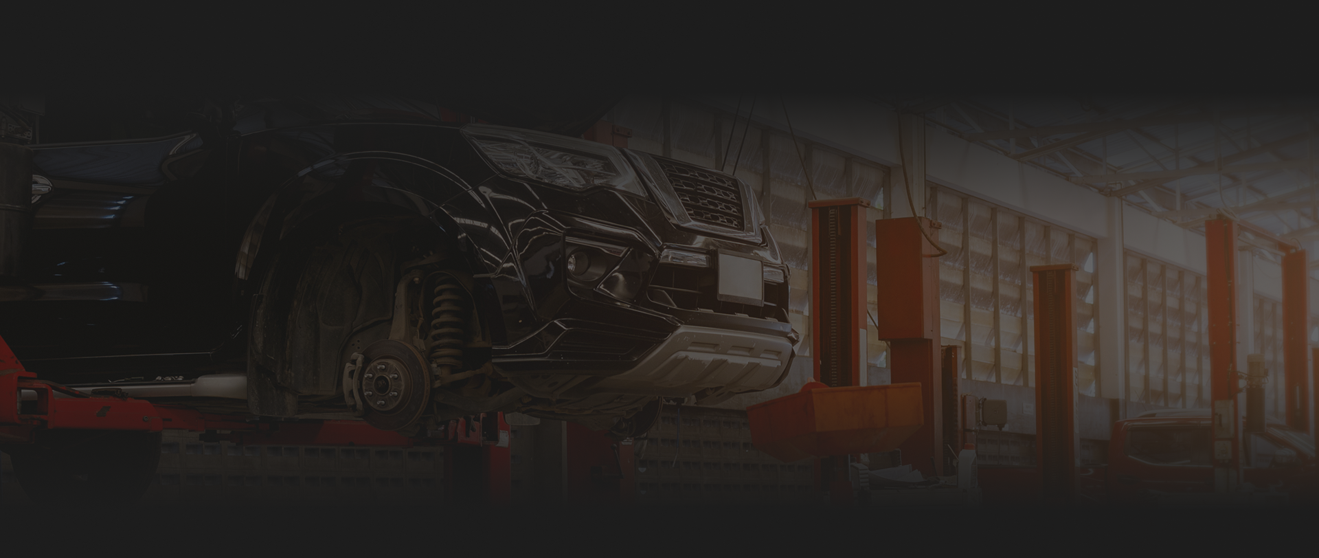 Car on a lift in a garage with orange support arms and a dark interior. | Destiny Vehicle Solutions