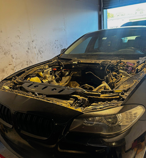 Black car with open hood, engine bay exposed, inside a garage. | Destiny Vehicle Solutions