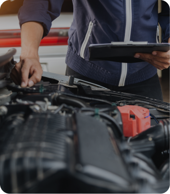 Mechanic inspecting a car engine while holding a clipboard. | Destiny Vehicle Solutions