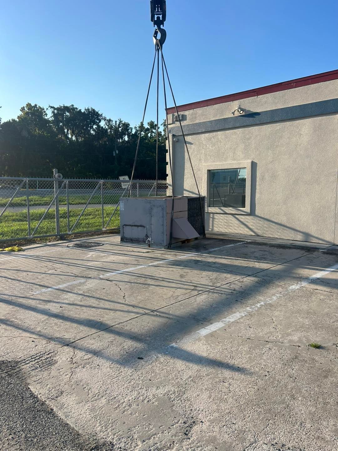 A crane lifts a large, gray electrical box next to a building on a concrete surface.