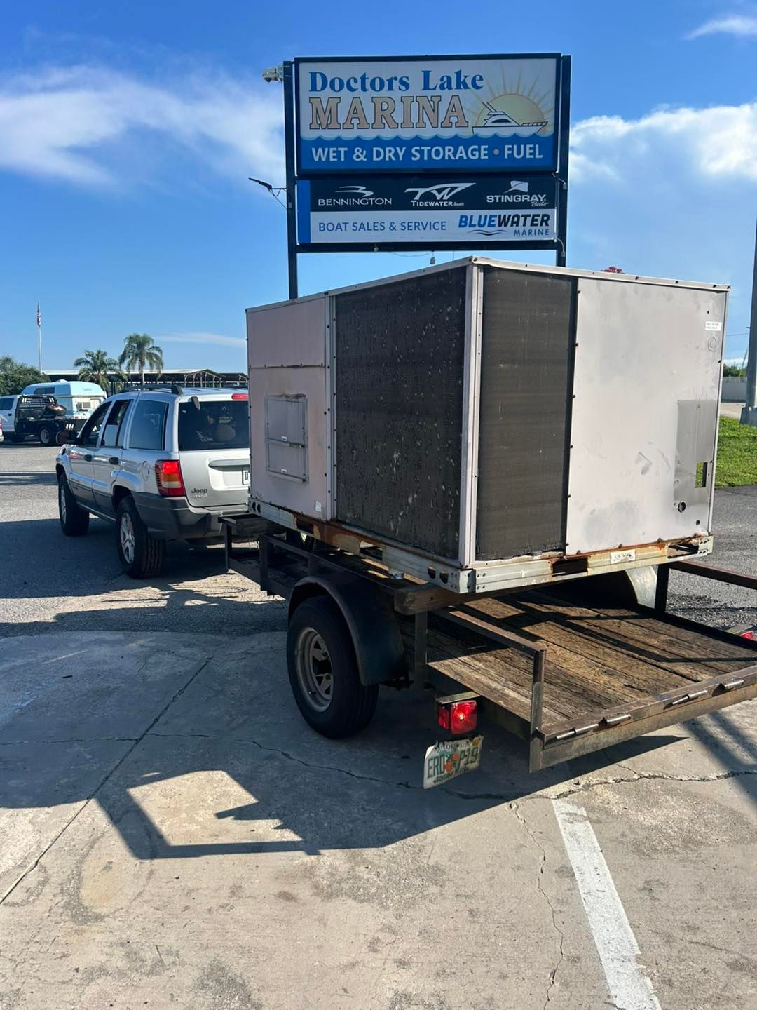 SUV towing trailer with large HVAC unit near marina sign.