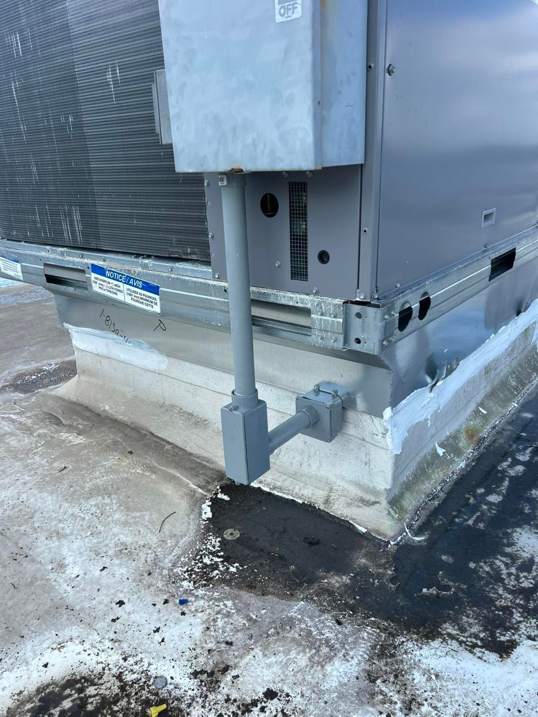 HVAC unit on a concrete rooftop with electrical conduit. Gray metal against a light gray base and dark stains.