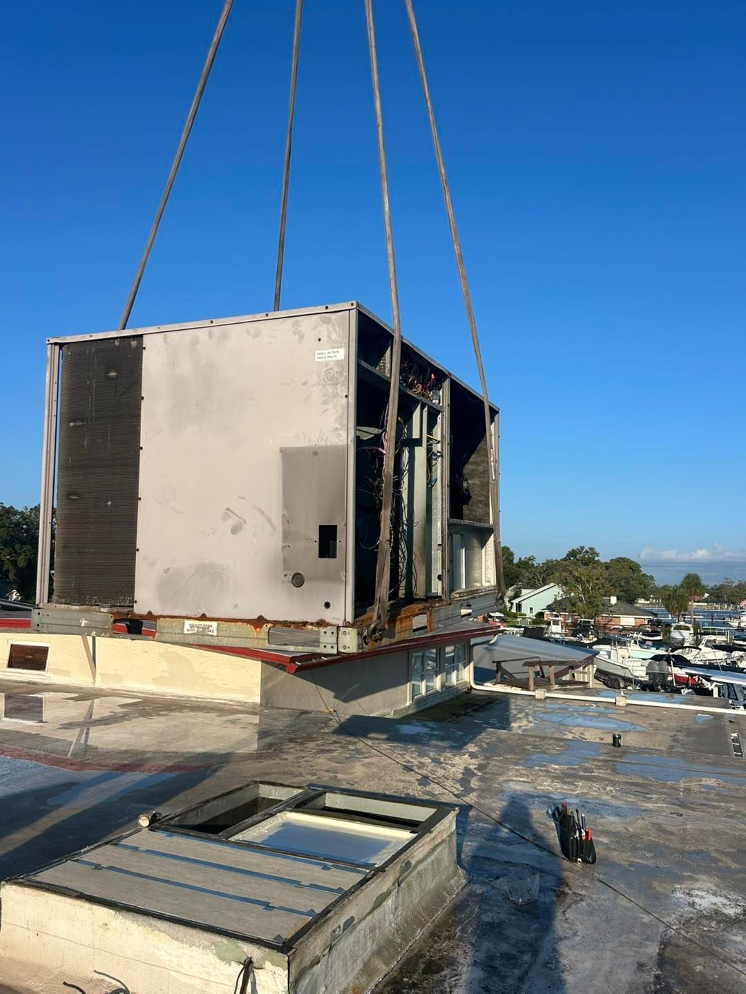 Large HVAC unit being lifted by crane off a rooftop, blue sky background.