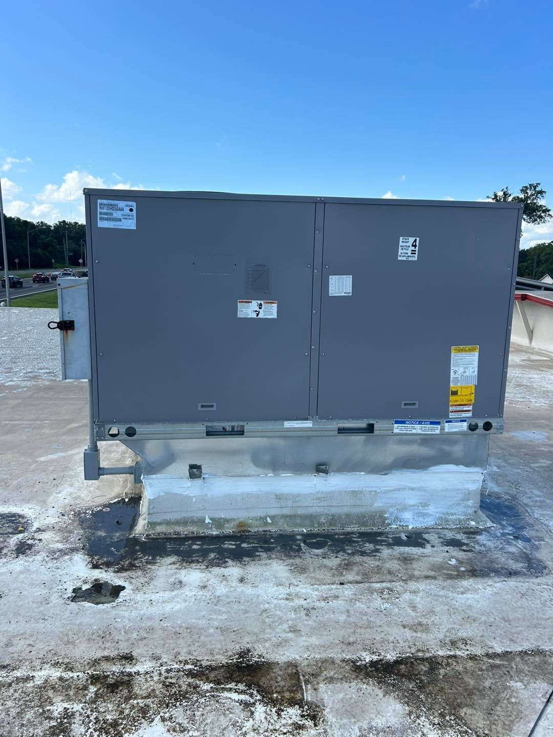 Gray rooftop HVAC unit on a weathered, white base, against a blue sky.