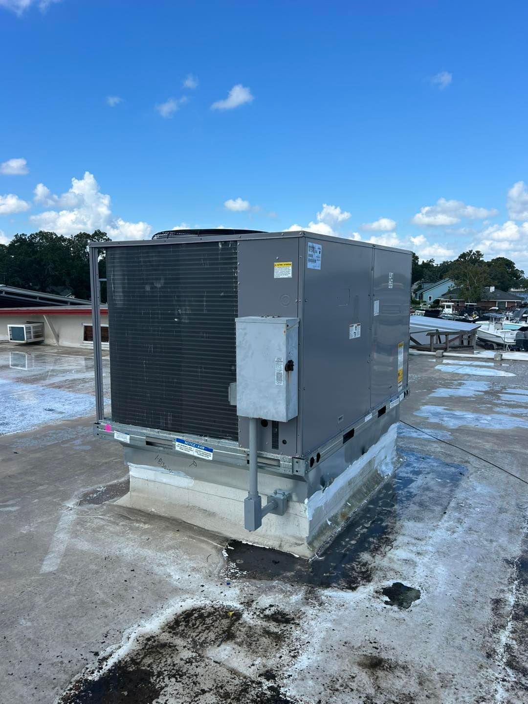 An HVAC unit on a flat roof under a blue sky with scattered clouds.